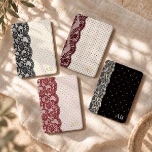 May include: Four rectangular notebooks featuring lace patterns and polka dots. Three have cream covers with black, burgundy, or red lace and gold AB initials. One has a black cover with white polka dots, white lace, and white AB initials.
