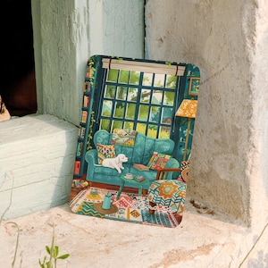Può includere: Una stampa rettangolare con un'illustrazione colorata di un accogliente soggiorno con un divano color ottanio, un cane bianco, una grande finestra, librerie e un tappeto a motivi. Il nome Jennie è scritto in corsivo bianco in basso a destra.