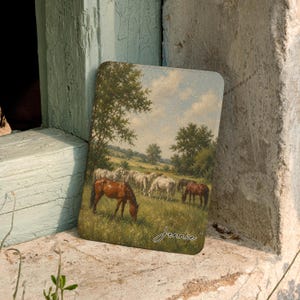 May include: A rectangular plaque featuring a pastoral landscape painting of a herd of horses grazing in a green field with trees under a cloudy sky. The name Jennie is written in white cursive script in the bottom right corner of the image.