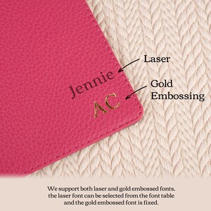 以下が含まれることがあります： ピンクの革製の財布のクローズアップ。財布には「Jennie」という名前と「AC」というイニシャルが金で刻印されています。財布の上には「レーザー」と「金箔押し」という文字が書かれています。