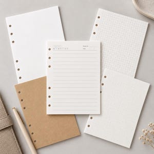 May include: A collection of five loose-leaf planner paper inserts with six-hole punches along the left side. The set includes one blank white sheet, one grid-patterned white sheet, one lined white sheet with date fields, one brown kraft sheet, and one dotted white sheet.