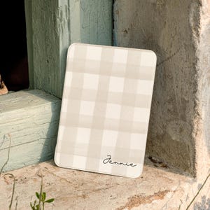 May include: A rectangular board featuring a light beige and white checkered pattern. The surface has rounded corners and the name Jennie is printed in a black cursive script in the bottom right corner of the board.