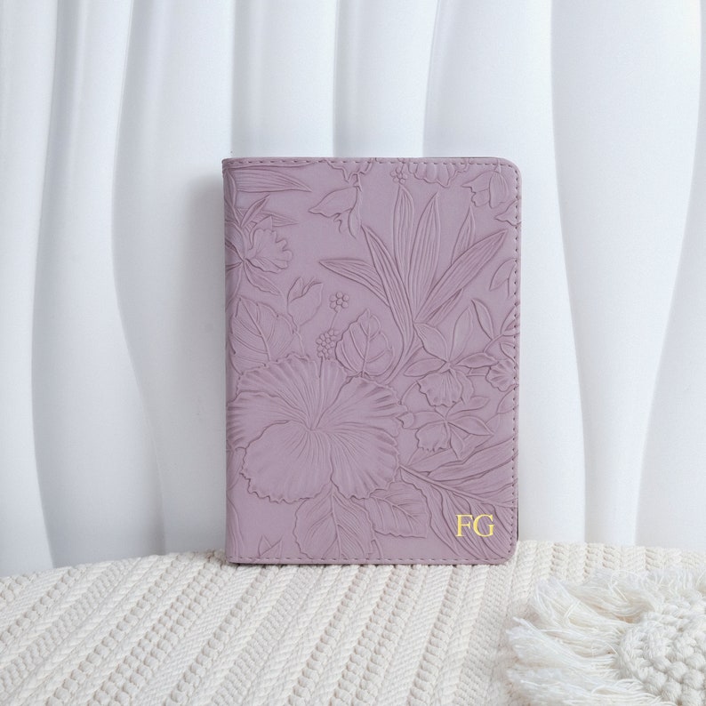 以下が含まれることがあります： ラベンダー色の革製のジャーナルで、花柄がエンボス加工されています。ジャーナルの表紙には、金色のエンボス加工で「FG」のモノグラムが施されています。