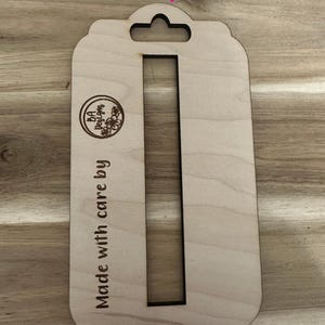 May include: A wooden cutout of a tag with a hole at the top for hanging. The tag has a rectangular shape with a vertical slot in the middle. The text "Made with care by BA Designs" is engraved on the left side of the tag. The text "SVG file" is at the top of the image and "Digital File Only!" is at the bottom of the image.