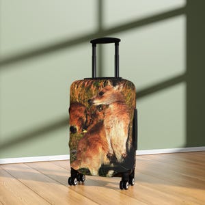 Peut inclure: Une valise à roulettes avec une image détaillée de wallabies roux dans un champ herbeux. Le bagage a une poignée et des roues noires. L'image des wallabies couvre toute la face avant de la valise.