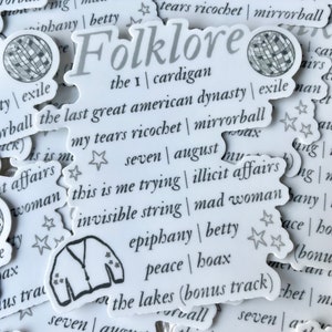 May include: A collection of white stickers with black text and illustrations. The stickers feature song titles and lyrics from the album "Folklore" by Taylor Swift. The stickers include titles like "the 1", "cardigan", "exile", "mirrorball", "invisible string", "mad woman", "epiphany", "betty", "peace", "hoax", "seven", "august", "this is me trying", "illicit affairs", and "the lakes (bonus track)".