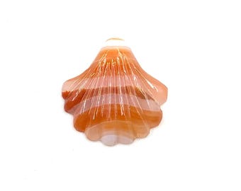 Puede incluir: Un colgante de concha de ágata tallada en tonos naranja y blanco. La concha está detallada con líneas intrincadas y un acabado liso y pulido.