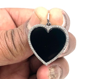 Puede incluir: Un colgante en forma de corazón negro con un halo de diamantes. El colgante es de plata y tiene un centro de ónix negro.