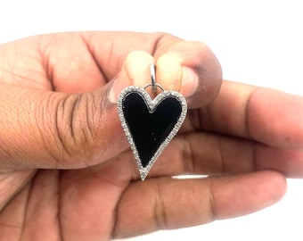 Puede incluir: Un colgante en forma de corazón negro con un borde de diamantes. El colgante está hecho de plata y tiene un acabado de esmalte negro.