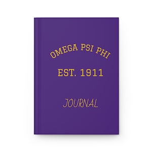 May include: A purple journal with gold lettering. The cover features the text "OMEGA PSI PHI EST. 1911 JOURNAL". The journal is rectangular and appears to be a hardcover book.