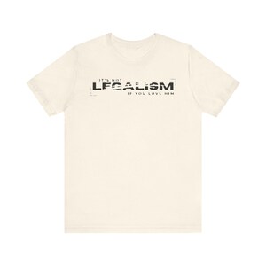 May include: Cream-colored t-shirt with the text "IT'S NOT LEGALISM IF YOU LOVE HIM" in black. The text is centered and has a distressed, textured appearance, giving it a vintage look. The shirt is made of a soft material.
