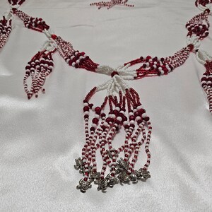 May include: A white and red beaded necklace with silver turtle charms. The necklace is made of small beads and has a tassel design.