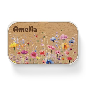 May include: A white lunchbox with a wood-grain design and a colorful floral pattern. The lunchbox has the name "Amelia" written on the front.