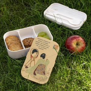 May include: A white lunchbox with three compartments, filled with cookies and grapes. The lid is open and features a wood-like design with a Japanese-inspired illustration of a woman looking in a mirror. The text on the lid reads "Friendship mirrors the beauty of shared dreams, the strength of shared struggles, and the joy of shared laughter."