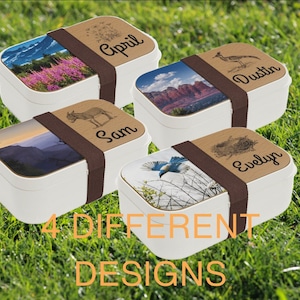 May include: Four different designs of personalized lunch boxes with various nature-themed images and names on the lids. The lunch boxes are white with brown straps.