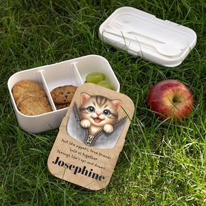 May include: A brown lunchbox with a cute cartoon cat peeking out of a zipper. The lunchbox has the text "Just like zippers, true friends hold us together through life's ups and downs. Josephine" printed on it.