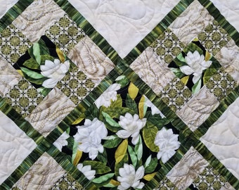 May include: A quilt with a diamond pattern featuring white flowers on a black background, surrounded by green and white patterned fabric.