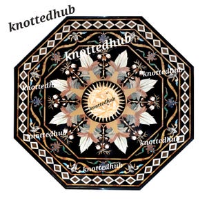 Puede incluir: Encimera de mesa octogonal de mármol negro con un intrincado diseño floral. El centro presenta un patrón de rayos de sol, rodeado de hojas y flores en tonos blancos, beige y marrón. El borde tiene un patrón geométrico y el texto "knottedhub".