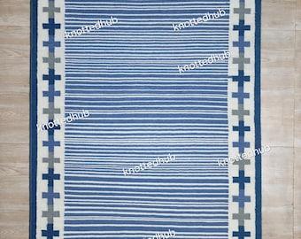 Op de afbeelding: Een rechthoekig blauw en wit tapijt met een streepjespatroon en een rand van kruisvormige ontwerpen. Het tapijt heeft een donkerblauwe rand en de tekst "knottedhub" is op verschillende plaatsen zichtbaar.