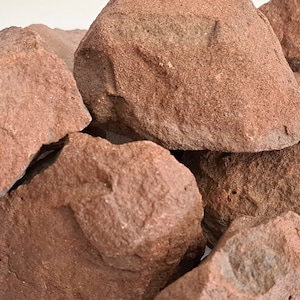 May include: A pile of rough, reddish-brown sandstone rocks. The rocks are various sizes and shapes, with a natural, unpolished finish.