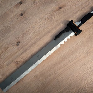 May include: A silver and black sword with a serrated edge and a black handle. The sword is lying on a wooden surface.