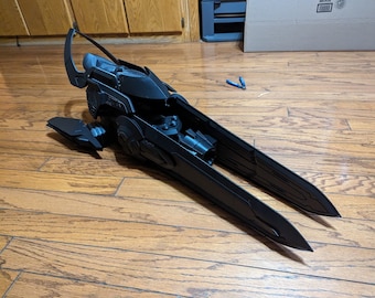 Può includere: Un modello di arma futuristica stampato in 3D, nero e dettagliato, con un'impugnatura curva e una lama lunga e affilata.
