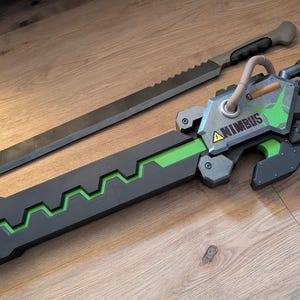Op de afbeelding: Een zwart en groen wapen met een zilveren blad en een groen-zwarte handvat. Het handvat heeft een zilveren plaat met het woord "ANIMBUS" erop. Het wapen is een rekwisiet voor cosplay of een filmset.