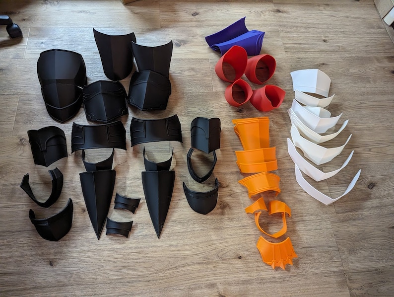 Op de afbeelding: Een verzameling 3D-geprinte kostuumstukken in zwart, wit, oranje en blauw. De stukken zijn gemaakt van plastic en zijn ontworpen om te worden gebruikt als onderdeel van een kostuum.