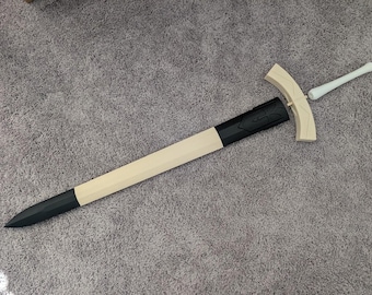 May include: A long, light-colored sword with a black tip and a black handle guard. The hilt and handle are white. The sword is lying on a gray surface.