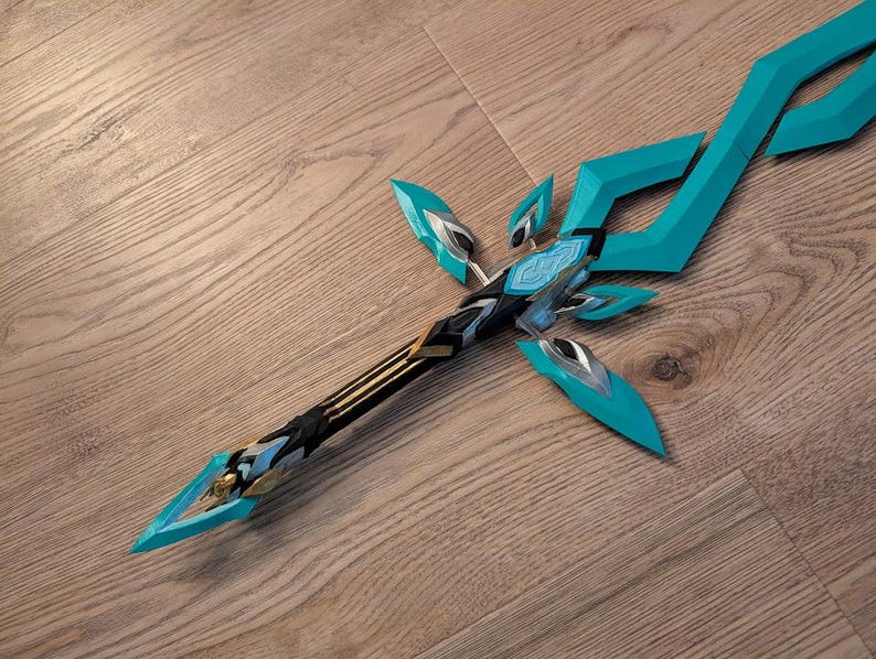 Op de afbeelding: Een teal en zwart fantasy zwaard met een gouden accent. Het zwaard heeft een scherpe punt en een gebogen lemmet.