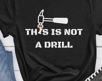 Op de afbeelding: Zwart T-shirt met een witte hamer en de tekst "THIS IS NOT A DRILL".