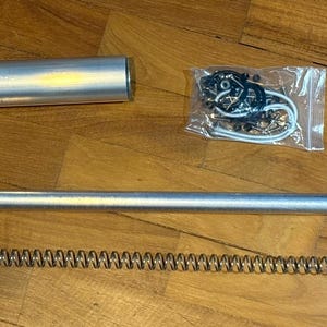 May include: An assortment of metallic hardware components, including a long, straight tube, a shorter cylindrical tube, a coiled spring, and a small bag of fasteners. The items are silver and appear to be new.