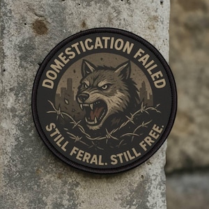 Może przedstawiać: Okrągła naszywka z ilustracją wściekłego wilka, otoczona drutem kolczastym i tłem miasta. Tekst brzmi: "DOMESTYKACJA ZAWIODŁA WCIĄŻ DZIKI. WCIĄŻ WOLNY."