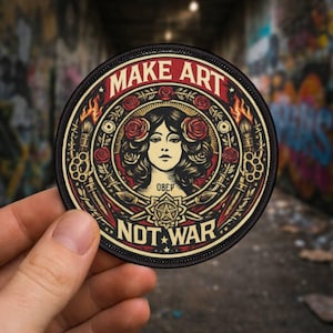 May include: A circular patch with the words "MAKE ART NOT WAR". The design features a woman's portrait with roses, surrounded by artistic tools and flames, in a vintage style, with a black border.