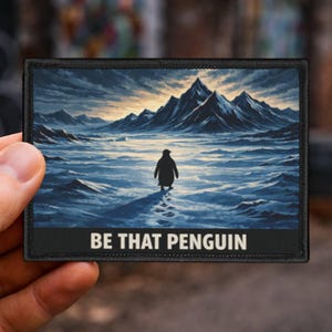Puede incluir: Parche rectangular con un pingüino caminando hacia montañas en un paisaje nevado. La imagen es en tonos de azul y gris, con el texto "BE THAT PENGUIN" en la parte inferior.