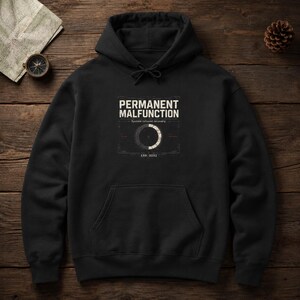 Könnte beinhalten: Ein schwarzer Kapuzenpullover mit einem weißen Grafikdruck auf der Brust. Der Text lautet PERMANENT MALFUNCTION, System refused recovery und ERR: 0092, begleitet von einem kreisförmigen Ladesymbol-Design mit dünnen Linien und Fadenkreuzen.