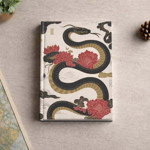 May include: A rectangular notebook with a cream-coloured cover featuring a black and gold serpentine dragon illustration. The design includes red floral accents, stylised clouds, and small black text characters printed on the front surface.