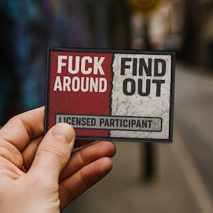 May include: Rectangular patch with the text "FUCK AROUND FIND OUT" in white letters on a red and white background. The bottom of the patch reads "LICENSED PARTICIPANT" in a grey box. The patch is held by a hand.