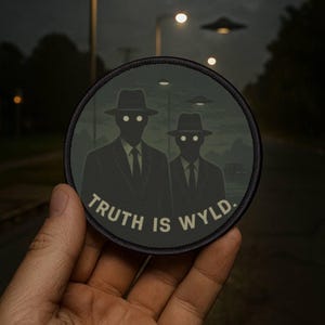 Può includere: Toppa rotonda con due figure in abito e cappello con occhi luminosi, e la scritta "TRUTH IS WYLD." Lo sfondo mostra una strada, lampioni e UFO. La toppa è verde scuro e nera.