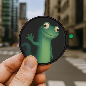 Pode incluir: Um patch redondo com um lagarto de desenho animado acenando. O lagarto é verde com olhos grandes e está em um fundo escuro. O patch tem uma borda preta. O patch é segurado em frente a uma rua da cidade.