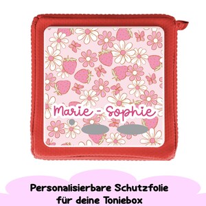 May include: Red protective case with a pink and white floral design featuring strawberries and butterflies. The case has the names "Marie - Sophie" printed on it.