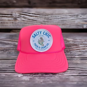 May include: Pink trucker hat with a white patch that says "Salty Chic Malibu Est. 2023 Tuck & Char Co. Tides, Waves & Freedom"
