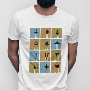 Puede incluir: Camiseta blanca con una cuadrícula de ilustraciones de naves espaciales negras sobre cuadrados de colores. Los diseños muestran varias naves espaciales, cada una con una silueta única y una estela blanca.