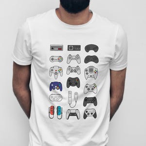 May include: White t-shirt with a graphic of various video game controllers. The controllers are in different shapes and colours, representing different consoles. A fun design for gamers, evoking nostalgia.