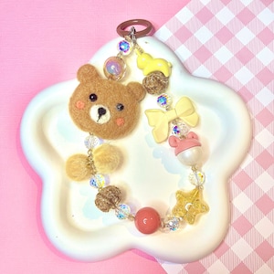 May include: A brown felt bear charm with a pink nose and black eyes, attached to a beaded keychain with a yellow star, pink bow, and other colorful beads.