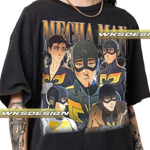 Puede incluir: Camiseta negra con un gráfico de personajes de estilo anime y el texto "MECHA MAN" en una fuente vintage. Los personajes están en varias poses, con rayos. La camiseta también tiene el texto "WKS DESIGN".