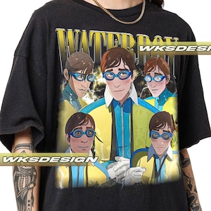 Puede incluir: Camiseta negra con un gráfico de dibujos animados de un hombre con gafas azules y el texto amarillo "WATER BOY". El gráfico tiene un esquema de color amarillo y azul. La camiseta también tiene el texto "WKS DESIGN".