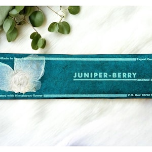 Könnte beinhalten: Eine türkisfarbene Schachtel mit weißem Text, der "Hand-Made in Nepal", "Decorated with Himalayan flower", "Export Quality", "JUNIPER-BERRY INCENSE STICK" und "P.O. Box 10762 Ktm." lautet. Die Schachtel hat auf der linken Seite ein weißes Blumendesign.