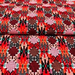 May include: Close-up of a vibrant fabric with a geometric pattern. The design features repeating diamond and rectangular shapes in red, orange, brown, pink, and black. The fabric is folded, showing the pattern's repeating nature.