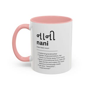 May include: White ceramic mug with a pink rim and handle. The mug features a black and white graphic with the word "nani" in Gujarati script and English, along with a definition of the word. The definition reads: "[naa-nee] noun 1. maternal grandmother 2. spoiler of grandchildren: her home is a home away from home 3. gives unconditional love, tells the best stories and makes the most delicious homemade meals 4. see also: "beautiful", "superwoman"